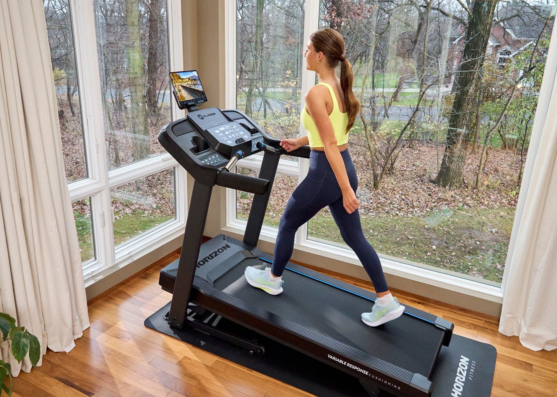 Woman walking on a Horizon T101 treadmill in a bright home gym