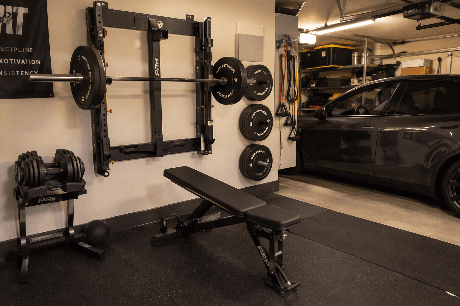 Compact garage gym with a wall-mounted folding squat rack, adjustable dumbbells, folding bench, wall plate storage, rubber mats, and a parked car sharing the garage