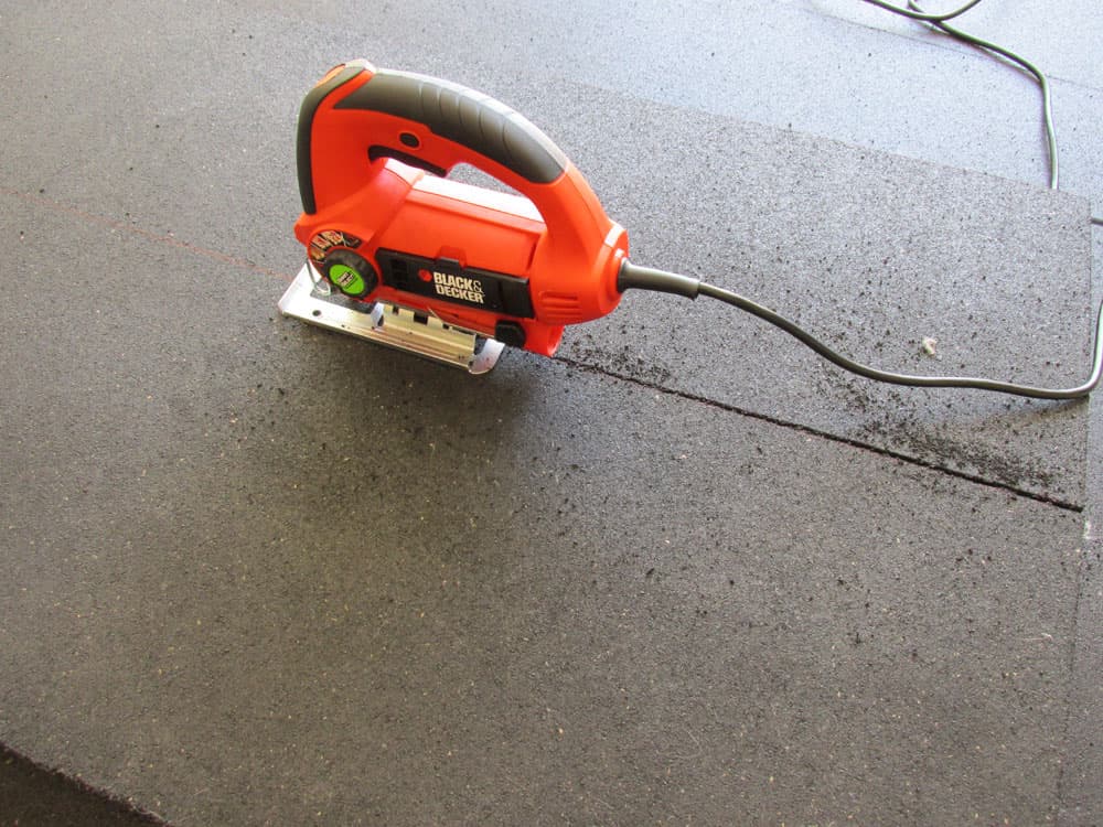 A utility knife cutting through a thick black rubber horse stall mat with the edge lifted