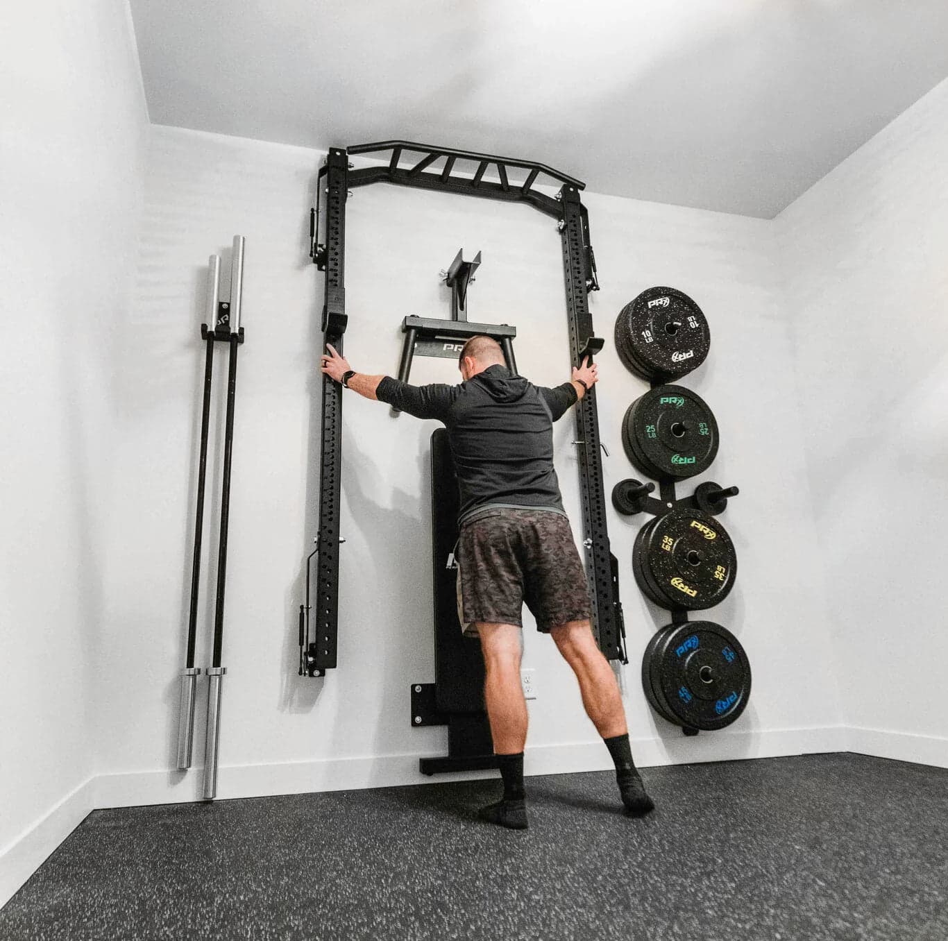 PRx Profile PRO foldable squat rack folded flush against a wall in a small home gym with a barbell stored on the rack