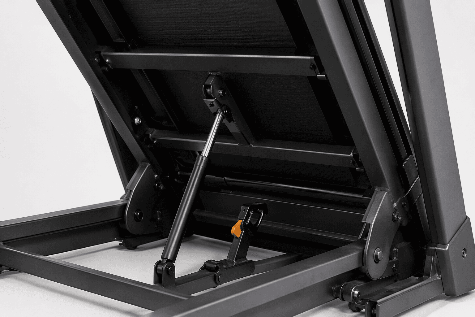 Close-up of a folding treadmill hinge, gas shock tube, deck latch, and frame hardware