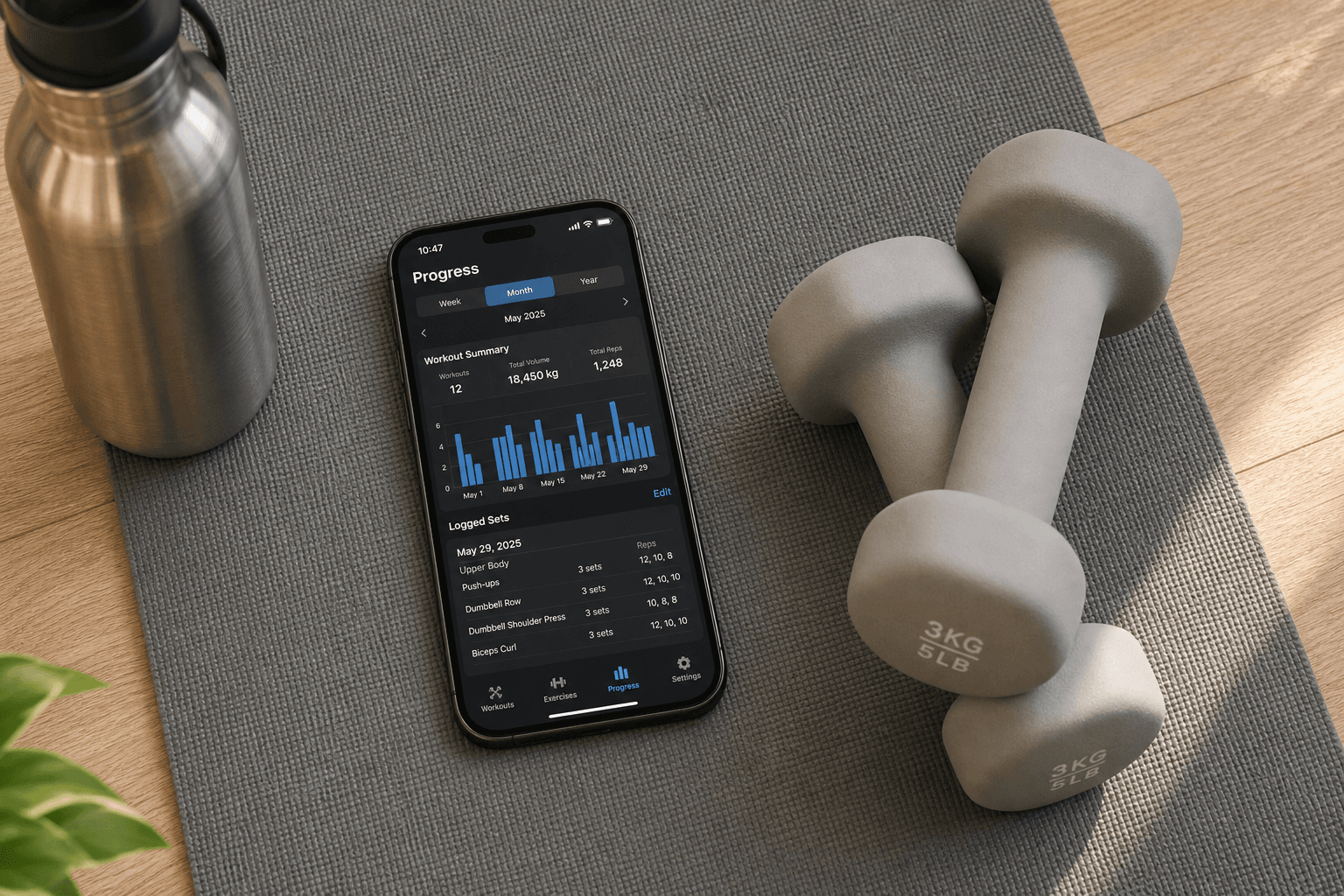 Top-down flat-lay photo on a grey yoga mat: a smartphone displaying a fitness app with visible workout progress charts and logged sets, next to a metal water bottle and two light dumbbells.