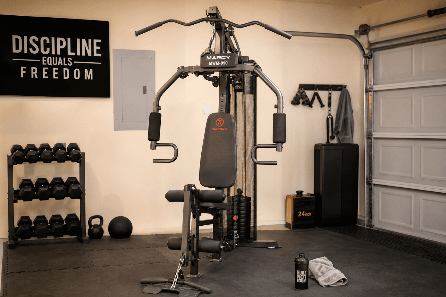 A Marcy MWM-990 150lb stack home gym in a finished garage with rubber flooring, showing the weight stack, lat bar, and press arms.