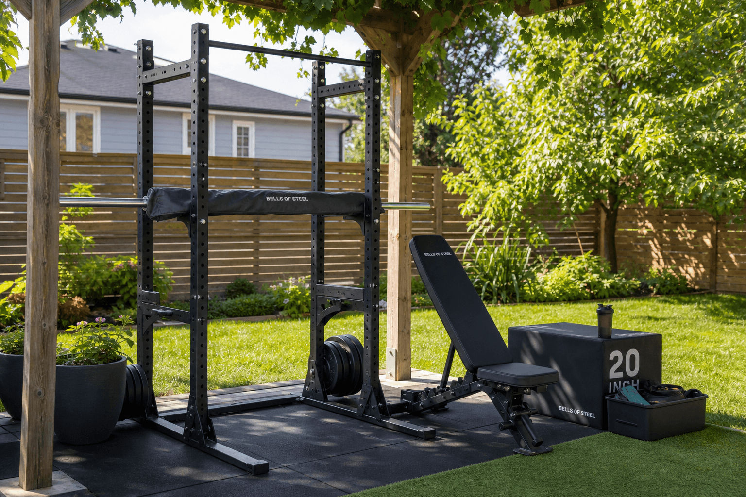 A residential backyard home gym setup with a powder-coated power tower, adjustable bench, and plyo box on rubber flooring under a pergola.