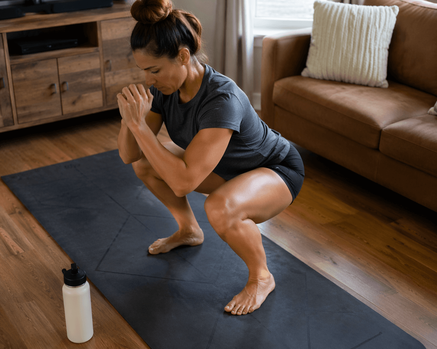 A person performing a deep bodyweight squat on a yoga mat in a home living room with natural light.