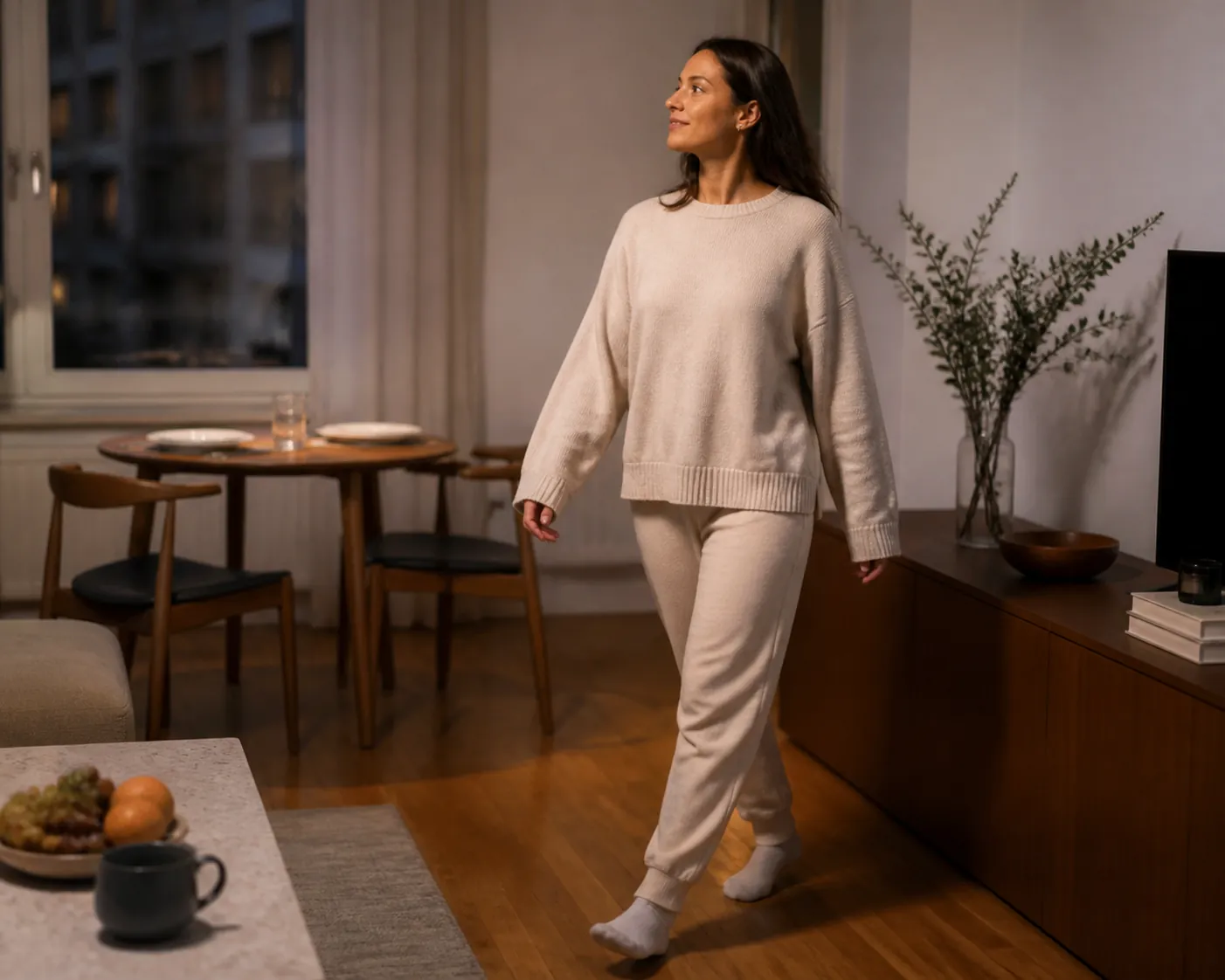 A relaxed person in socks walking across a small apartment living room after a meal