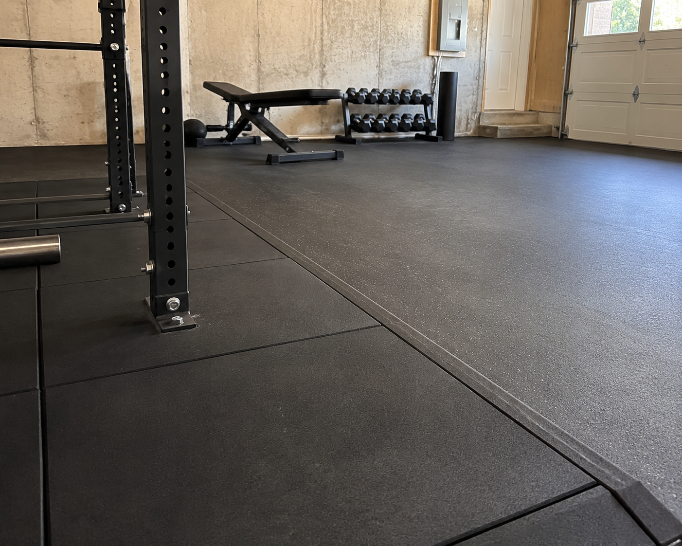 Garage home gym with thick stall mats at the power rack and thinner rolled rubber across the remaining floor