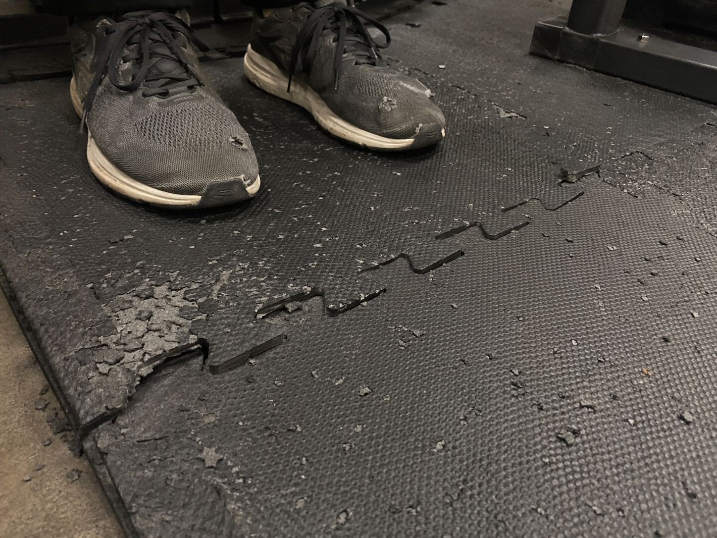 Worn EVA foam puzzle mat with peeling edges, surface damage, gray flecks, and a lifting seam