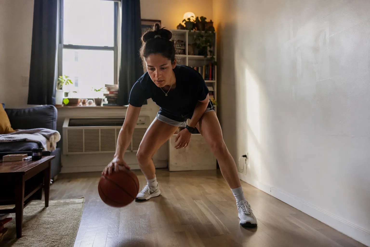 A basketball player dribbling low in a small apartment living room with furniture pushed aside