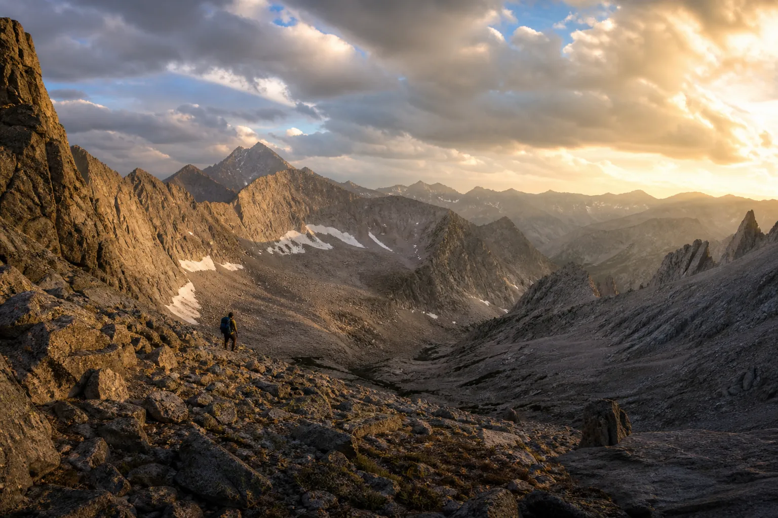 A lone hiker navigating rugged off-trail Wyoming alpine terrain with talus, scree, granite ridges, and distant mountain peaks