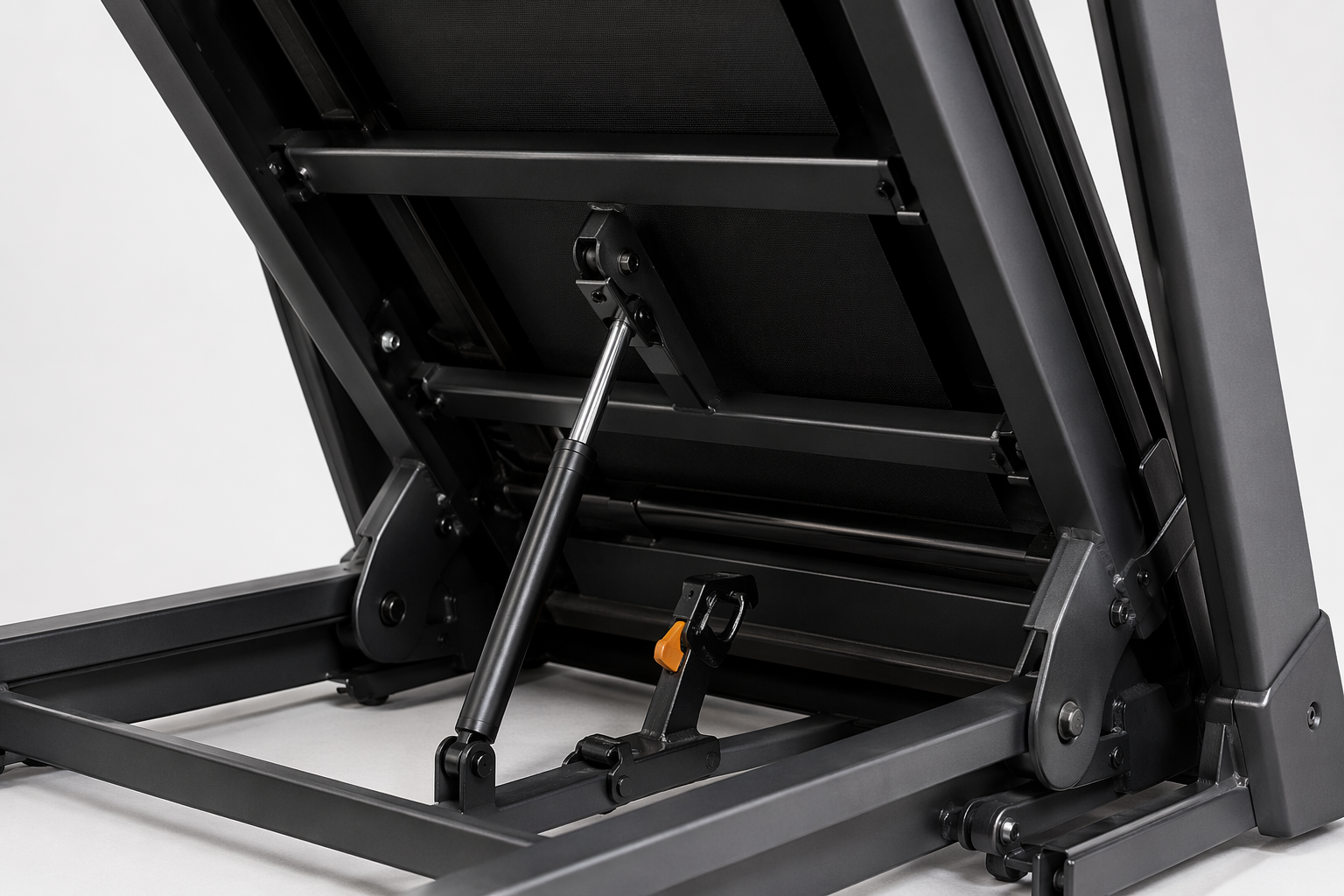 Close-up of a folding treadmill hinge, gas shock tube, deck latch, and frame hardware