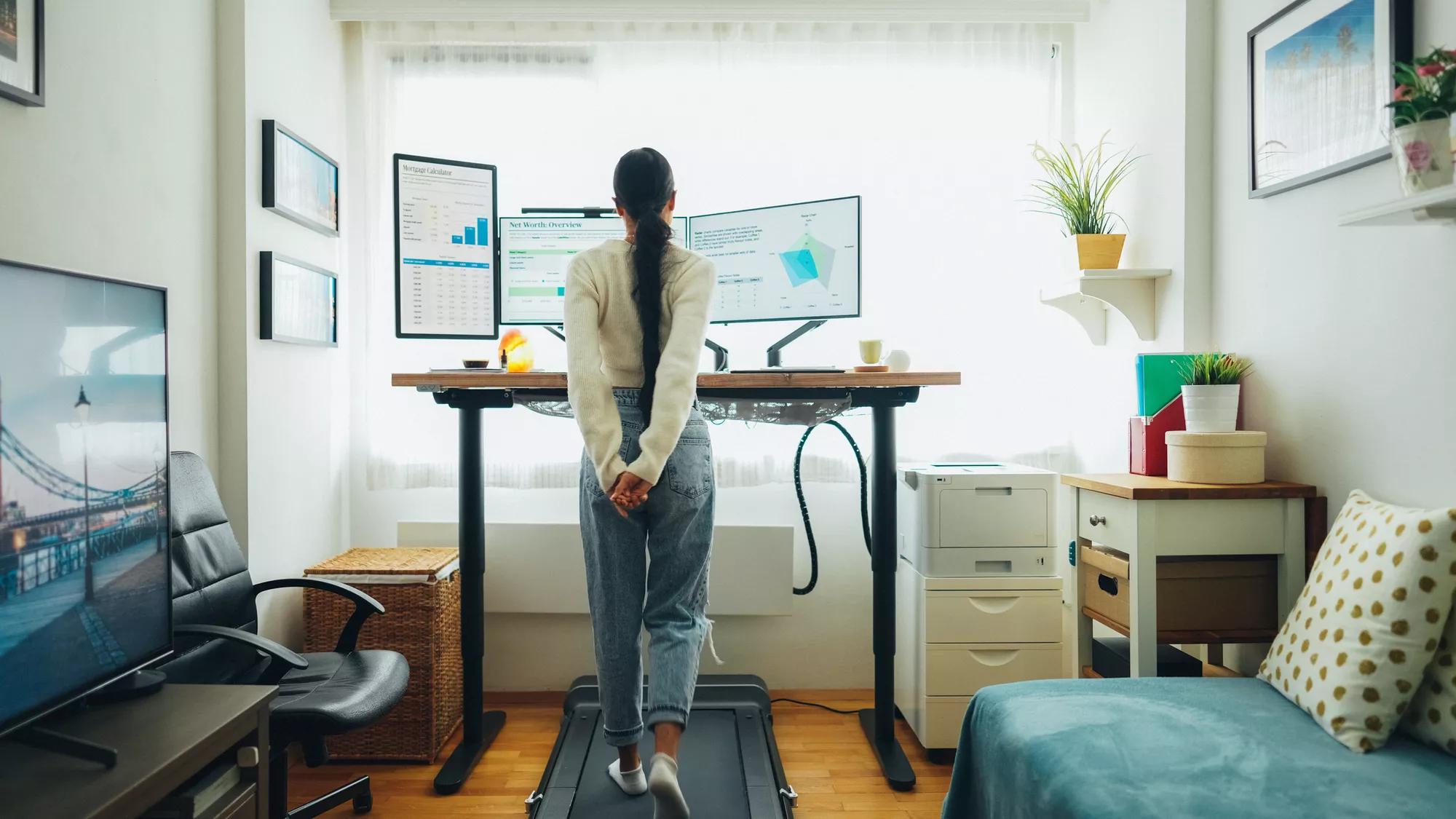 Person using a walking pad at a home office desk while working on a laptop