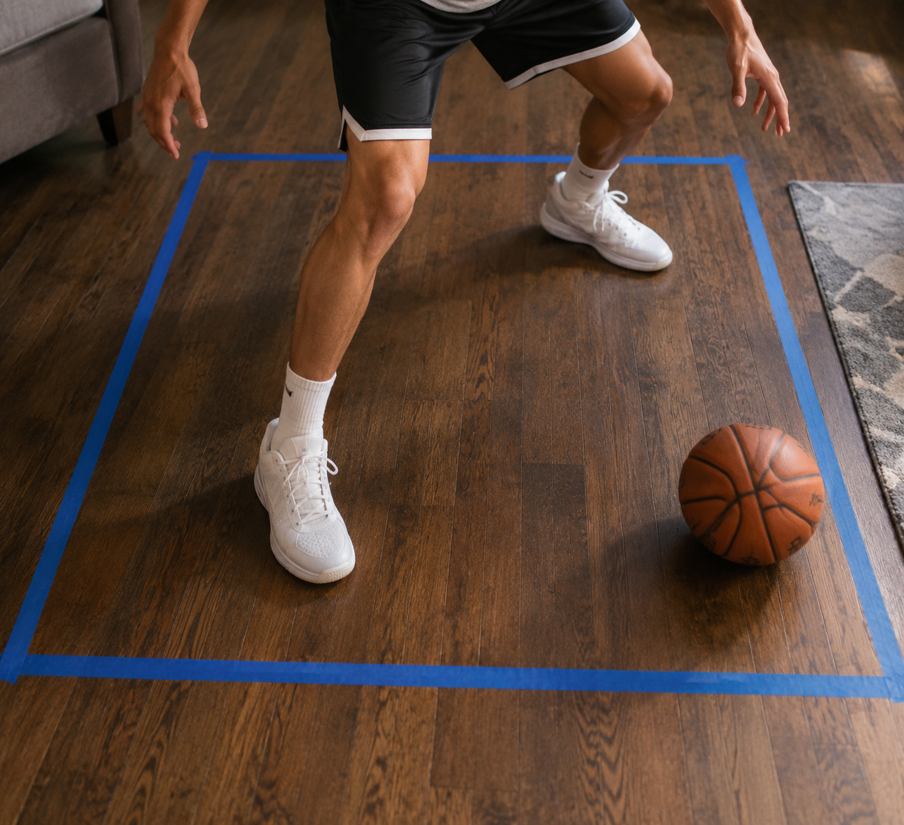 Overhead view of a 5x5 ft square on a wooden floor with a basketball player's feet in a wide defensive stance