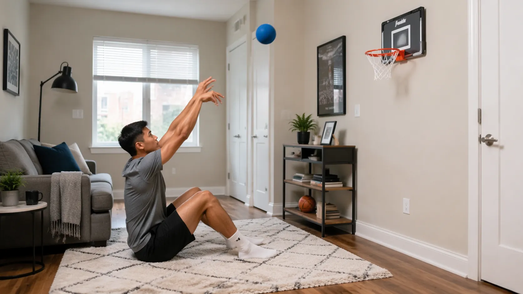 Person seated in a compact apartment practicing shooting form with a foam basketball toward an adhesive-mounted mini hoop