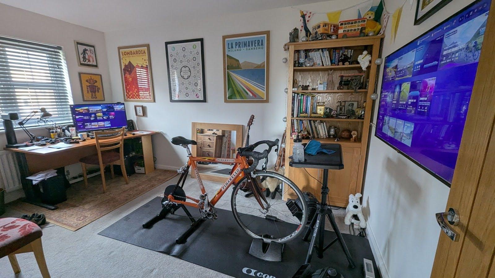 A road bike mounted on an indoor smart trainer in a compact home living space with a mat and towel.