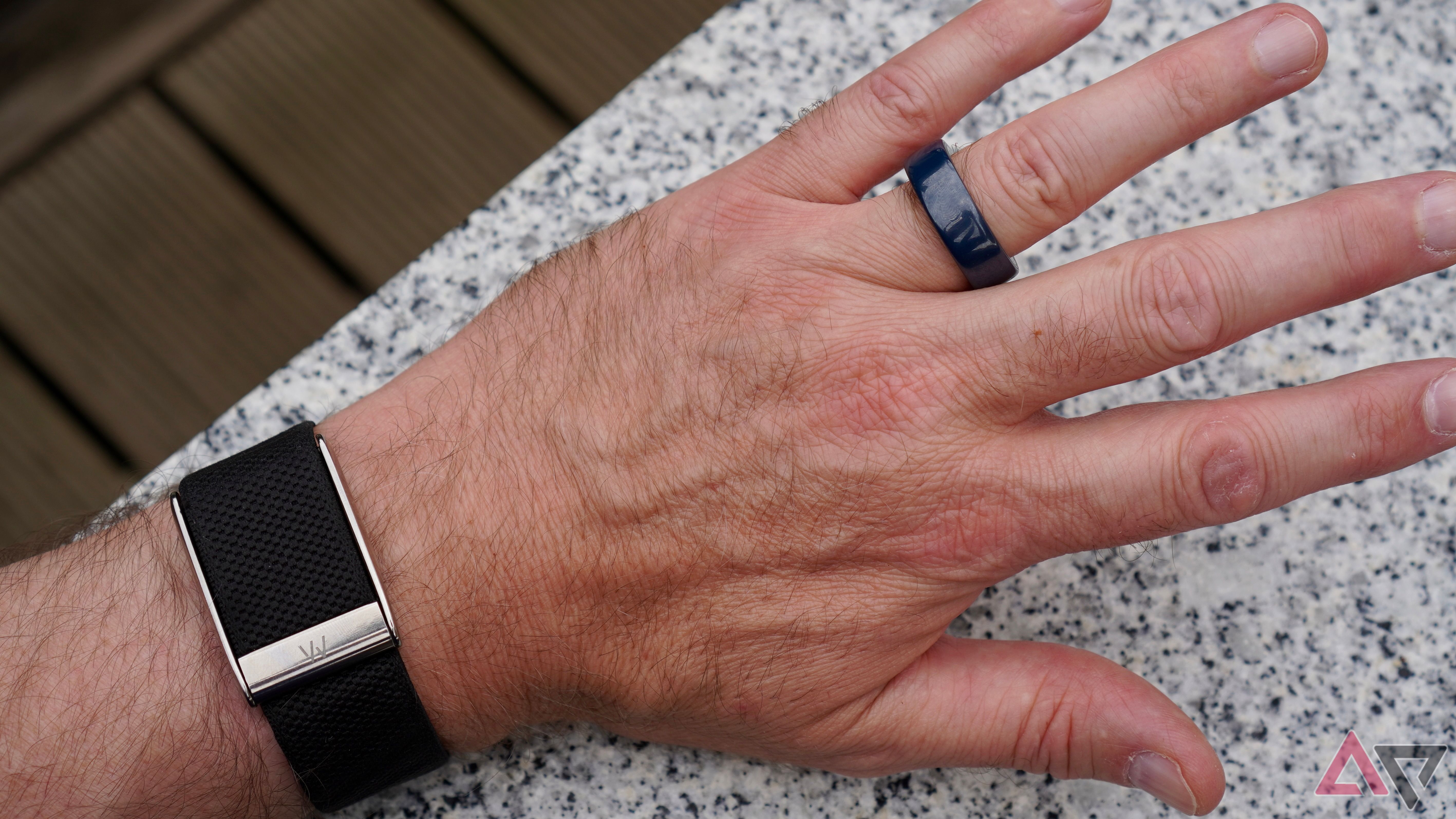 A hand wearing an Oura Ring and a WHOOP band at the same time