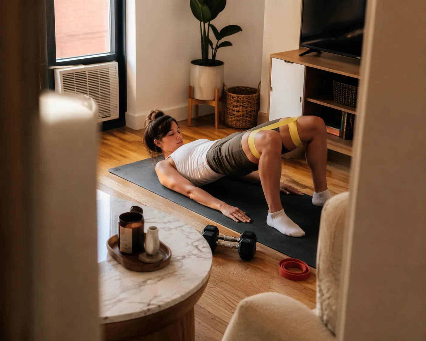 Runner doing a quiet strength exercise on a yoga mat in a compact apartment with bands and dumbbells nearby