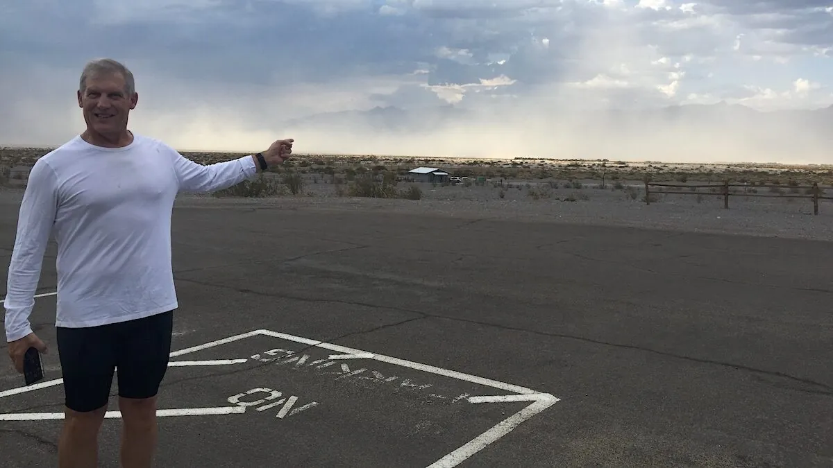 Older male runner in a white shirt and cap running along a desert highway under bright sunlight