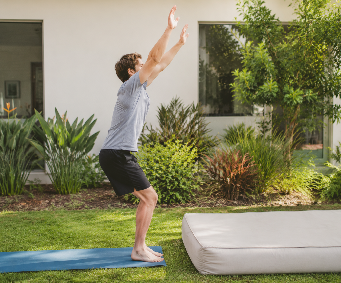 Person training for a backflip on a mat in a backyard with arms raised in preparation