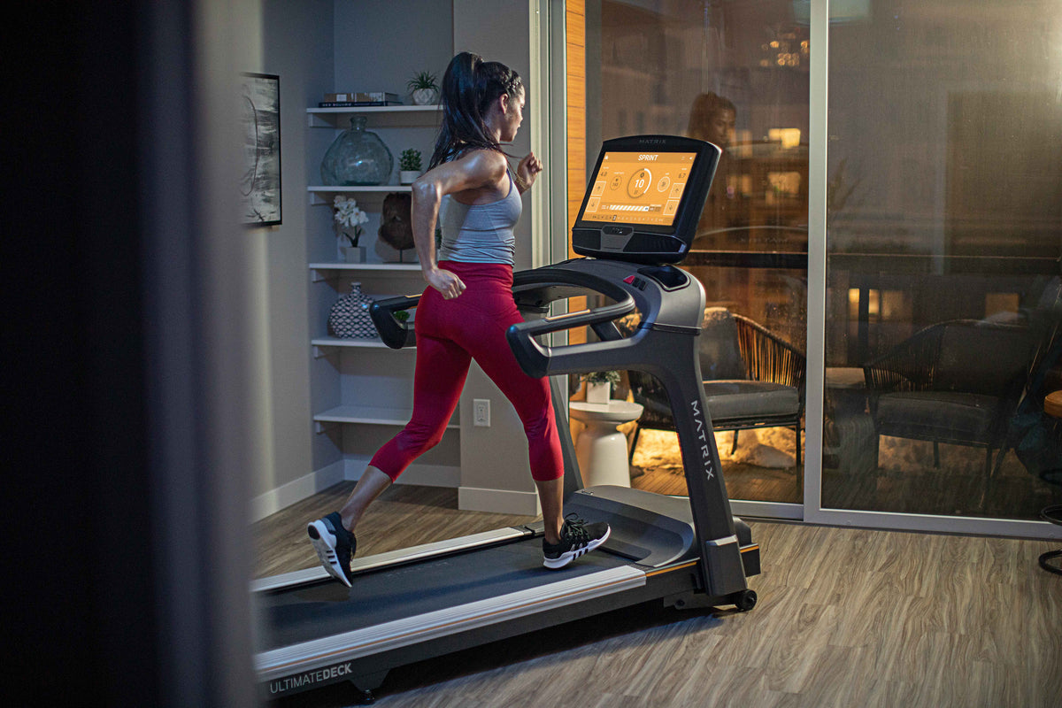 Matrix T75 treadmill in a home gym with a runner on the wide deck and touchscreen console visible