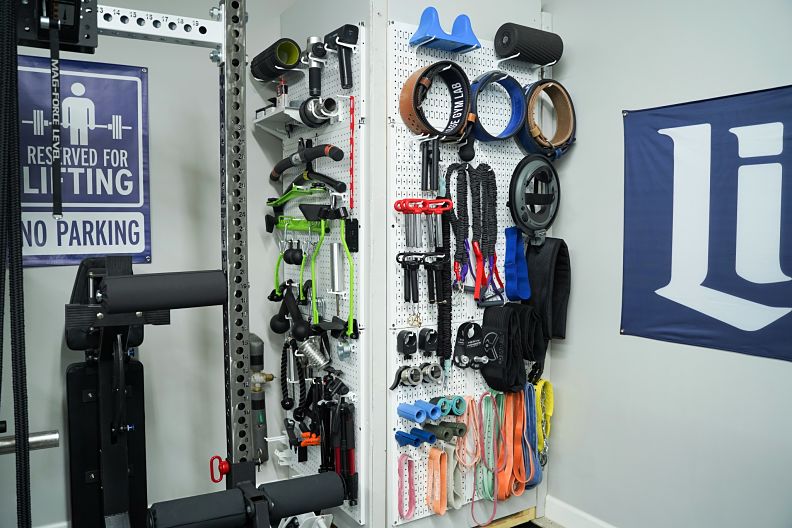 A Wall Control metal pegboard mounted on a garage wall, holding organized gym accessories including resistance bands, jump ropes, and small equipment on hooks and attachments.