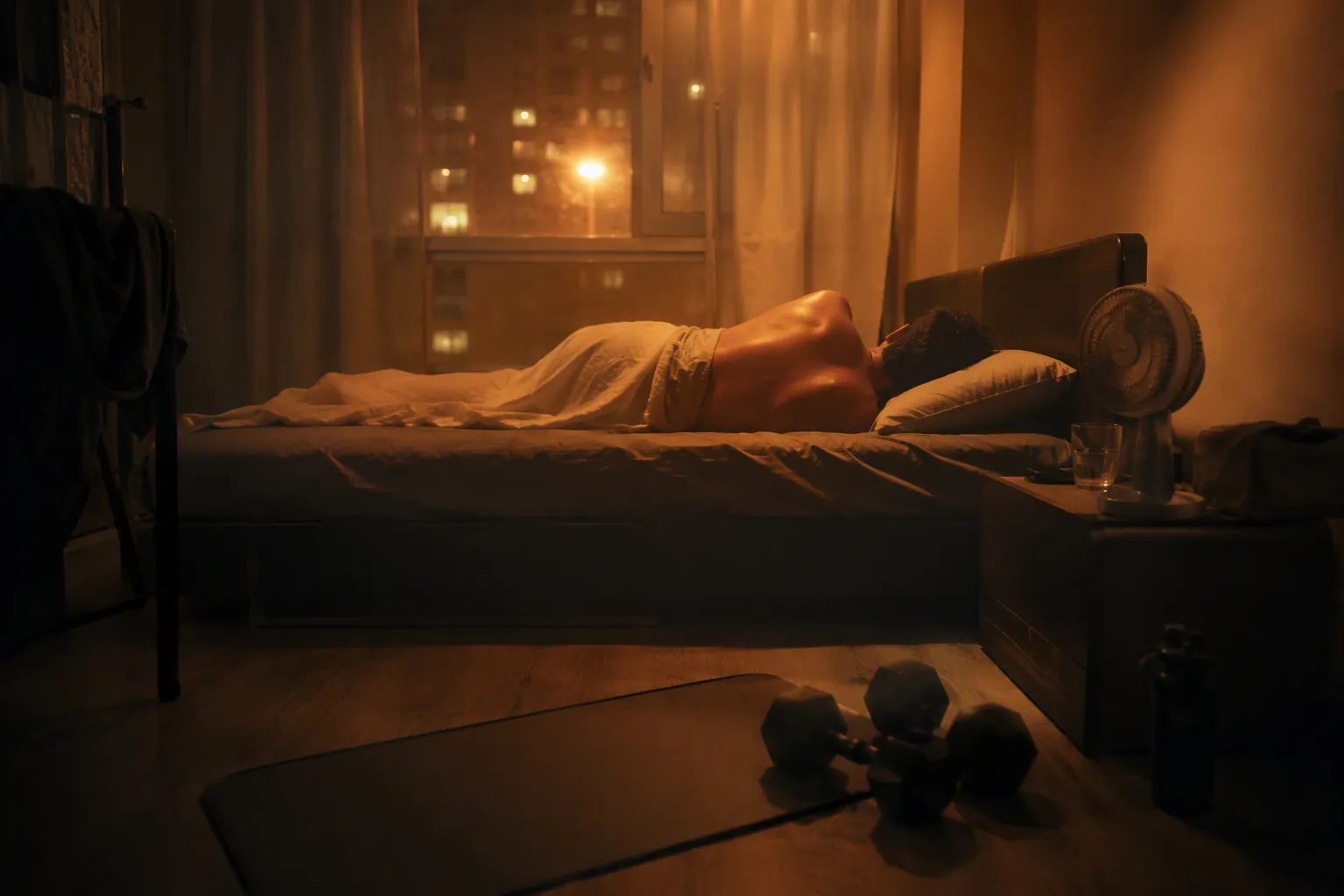 Hot apartment bedroom at night with dumbbells and an exercise mat in the foreground