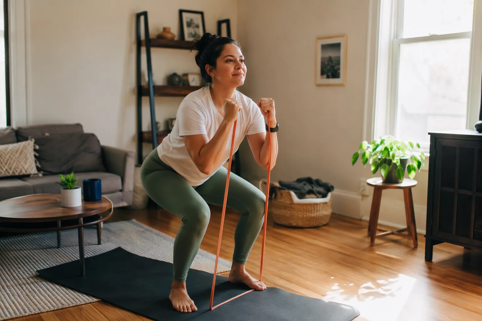 Person doing a resistance band squat in a sunlit living room