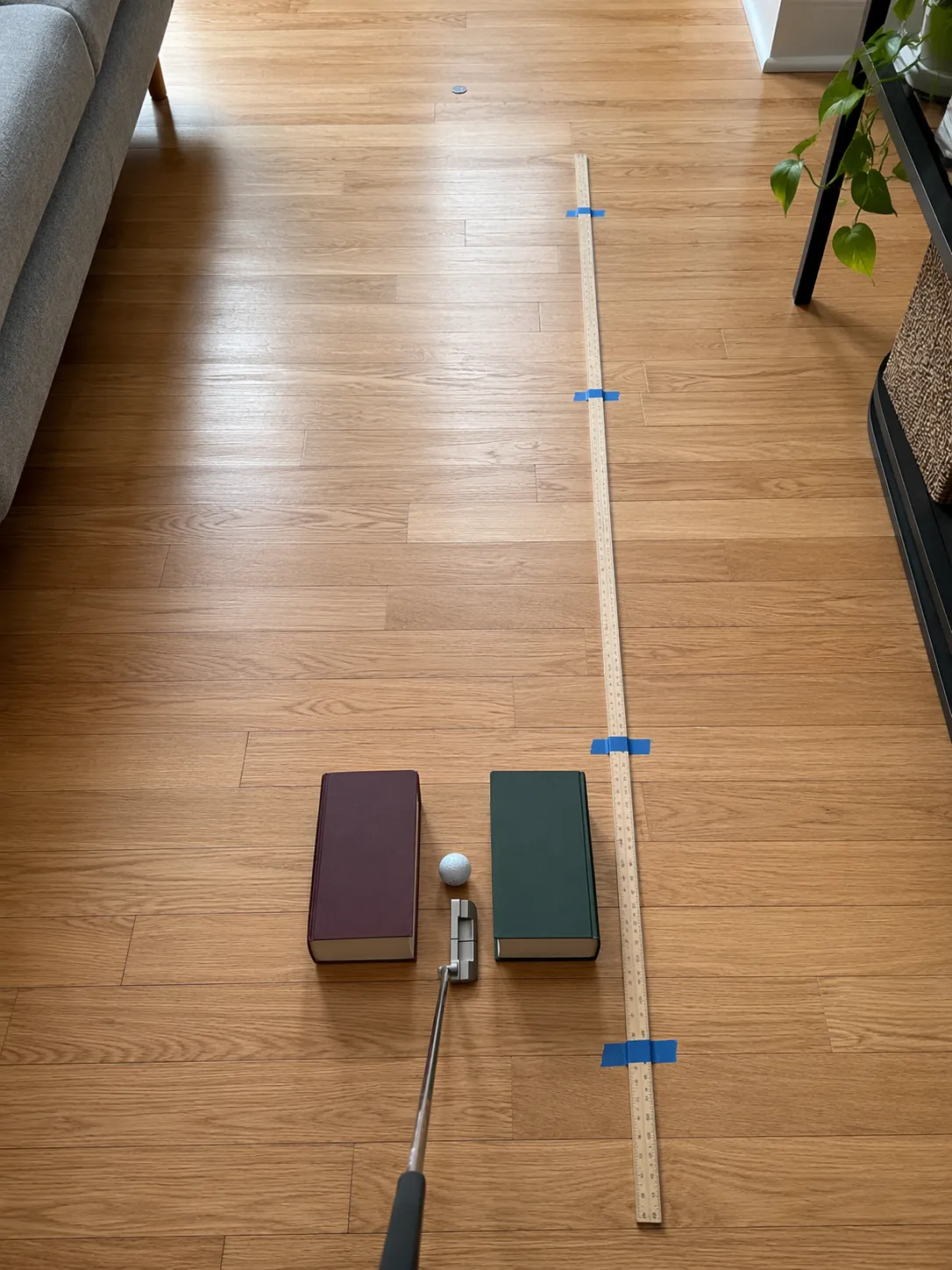 Indoor putting setup with books forming a channel, a coin target, and a yardstick on the floor