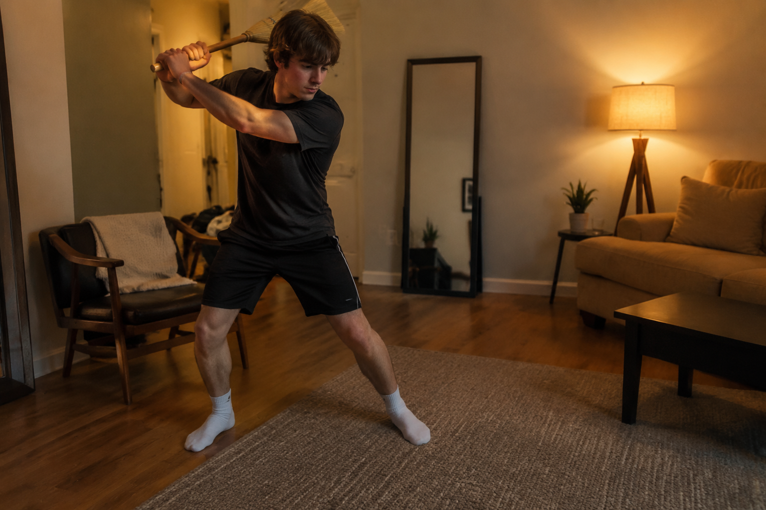 Player using a broomstick for safe swing work in a small living room with a mirror