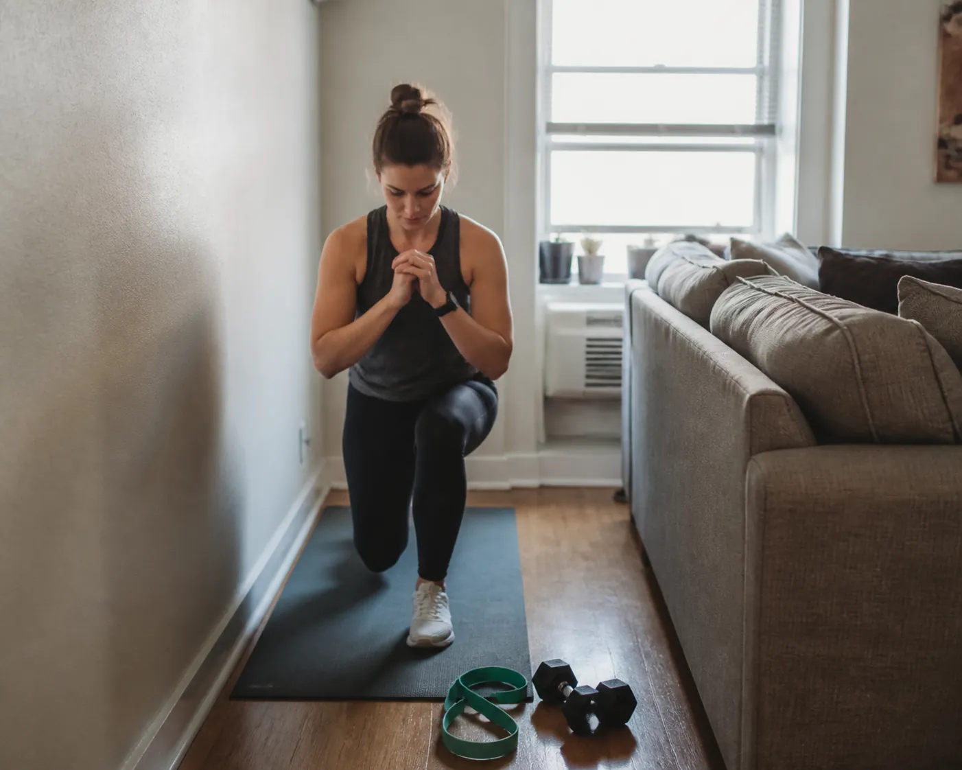 Person doing a bodyweight lunge on an exercise mat in a small living room with resistance band and dumbbells nearby